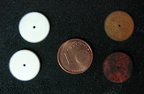 Zahnradrohlinge aus Elfenbein und aus Holz, daneben eine Münze zum Größenvergleich.
